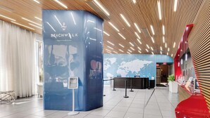 Een moderne lobby met een blauw receptiebalie, een wereldkaart aan de muur, en een rode sculptuur.