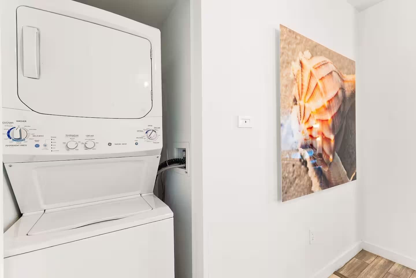 Eine weiße Waschmaschine in einem Raum mit Holzboden und einem an der Wand hängenden Bild.