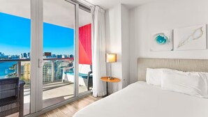 Hotelkamer met een groot bed, uitzicht op de stad, een balkon met een stoel en een tafel met een lamp.