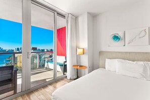 A hotel room with a large bed, a view of the city, a balcony with a chair, and a table with a lamp. - Bright 1BR - Sunset View -Beach Access (Hallandale Beach)
