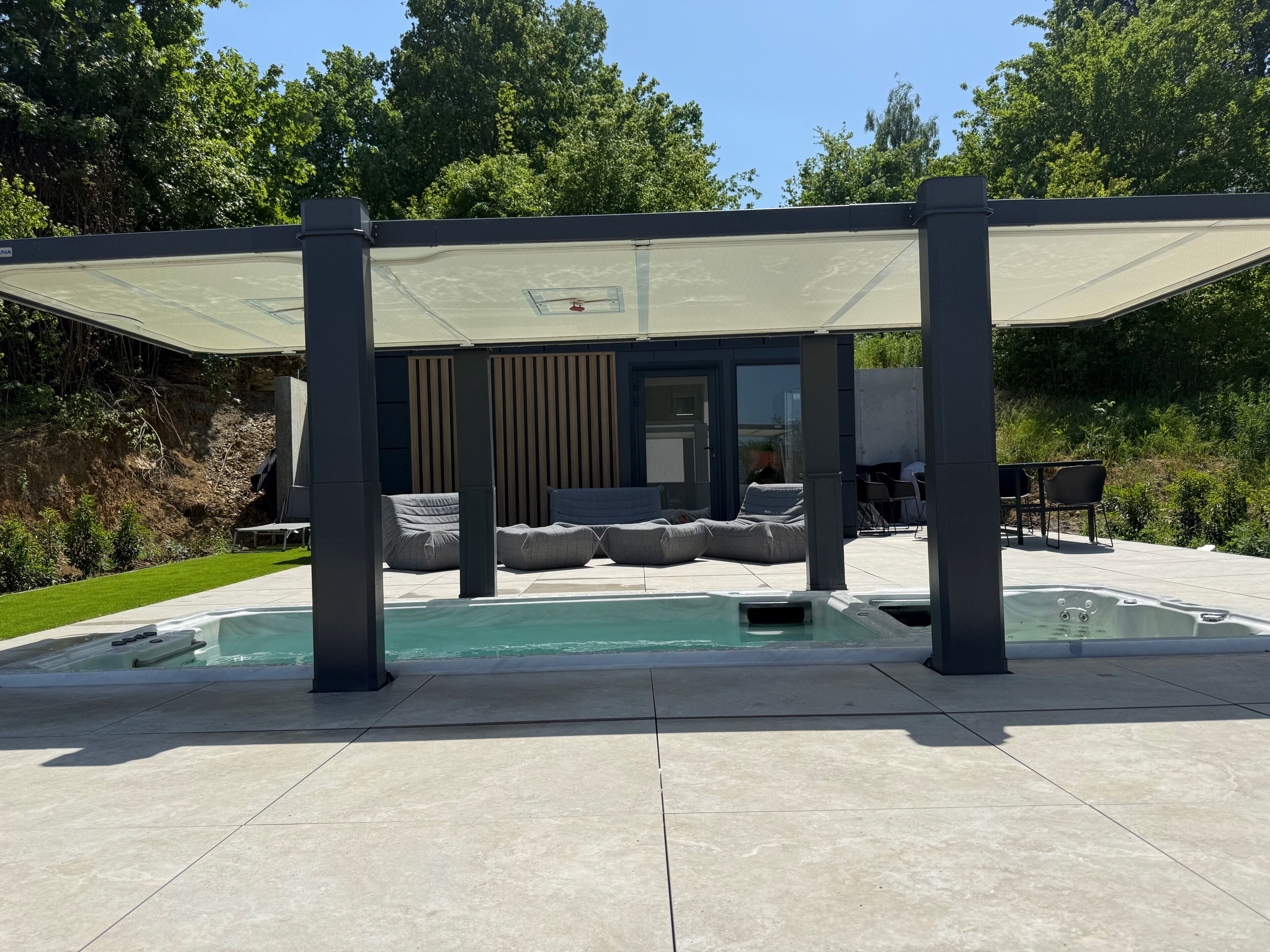 Un área de piscina moderna al aire libre, con zona de estar cubierta y un jacuzzi.