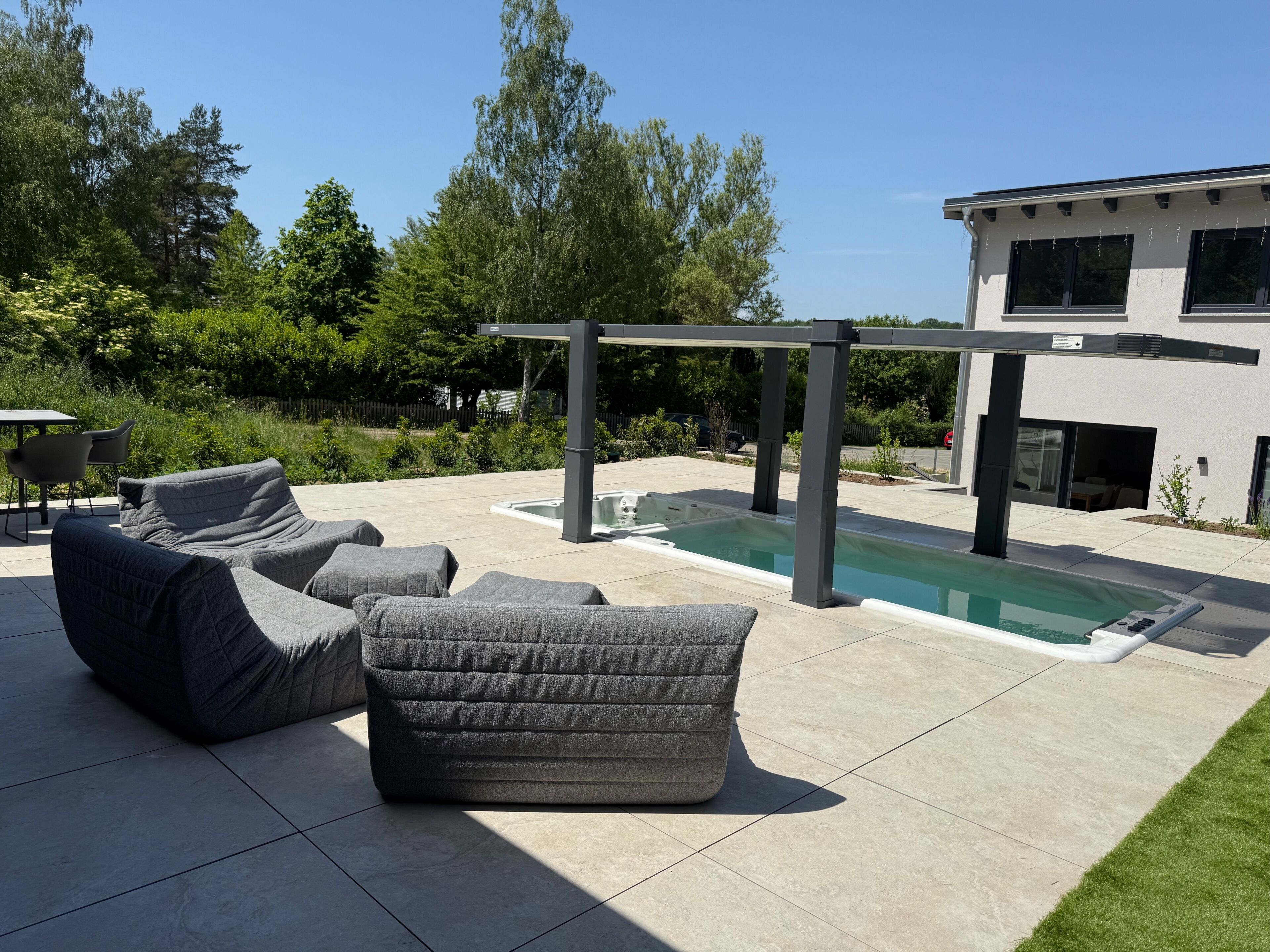 A modern outdoor patio with a pool, lounge chairs, and a pergola.