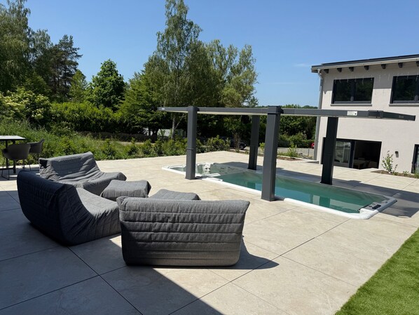 A modern outdoor patio with a pool, lounge chairs, and a pergola.