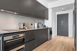 Eine moderne Küche mit dunklen Schränken, einem eingebauten Backofen, einer Kaffeemaschine und einer Waschmaschine.