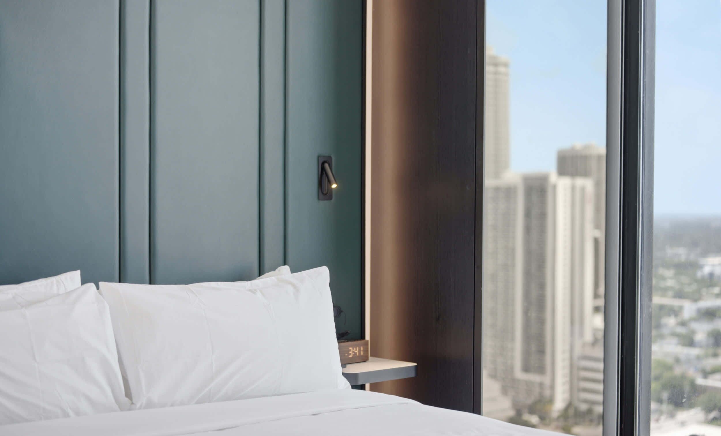 A hotel room with a bed, a nightstand, and a window with a city view.