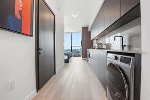 A modern kitchen with a built-in washer and dryer, a large window, and a view of the city. - Experience The Brand New E11EVEN Residences (Miami)