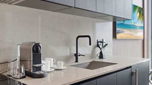 Una cocina moderna con cafetera, lavamanos y un cuadro de una playa.