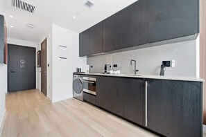 A modern kitchen with dark cabinetry, a built-in oven, and a stainless steel sink. - Stunning Studio Suite At The E11EVEN Residences (Miami)