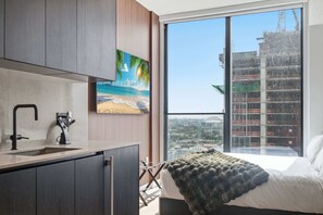 A modern bedroom with a large window, a bed with a blanket, a painting of a beach, and a view of a construction site. - Stunning Studio Suite At The E11EVEN Residences (Miami)