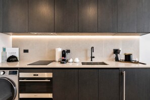 A modern kitchen with dark wood cabinets, a stainless steel sink, a coffee machine, and a dishwasher. - Rooftop Pool Condo in Downtown Miami w/ City Views (Miami)