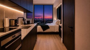 Een moderne hotelkamer met een keuken, een bed en een groot raam met uitzicht over de stad.