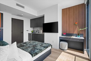 A modern bedroom with a bed, a desk, a TV, and a small kitchen area. - Elite E11EVEN Suite Rooftop Pool and City Views (Miami)