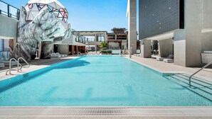 Ein Schwimmbecken mit einer großen Handskulptur, moderne Gebäude und ein klarer Himmel.