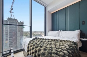 A modern bedroom with a large window, a bed with white linens, and a view of a construction site. - Indulge at E11EVEN Private Pool & Elite Gym (Miami)