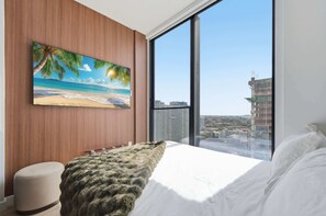 Ein Schlafzimmer mit großem Fenster, einem Strandbild und Blick auf eine Stadtlandschaft.
