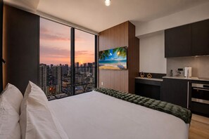 A modern hotel room with a large bed, a city view, a painting of a beach, and a kitchenette. - Indulge at E11EVEN Private Pool & Elite Gym (Miami)