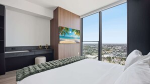 A modern bedroom with a large bed, a painting of a beach, and a city view through large windows. - Elevated Experience At The E11EVEN Residences (Miami)