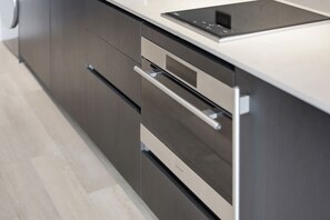 A kitchen with dark cabinetry, stainless steel appliances, and a white countertop. - Elevated Experience At The E11EVEN Residences (Miami)
