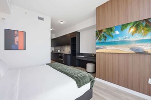 Ein modernes Hotelzimmer mit einem Bett, einem Bild einer Strandansicht und einer Küchenzeile im Hintergrund.
