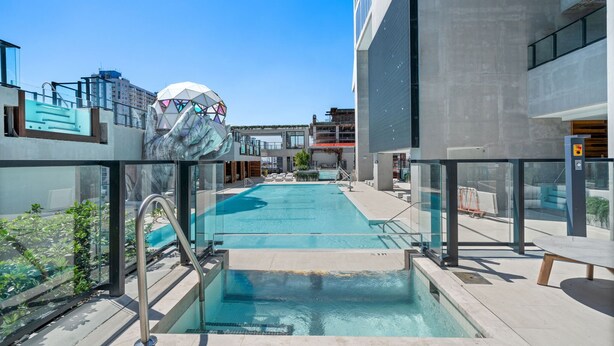 A rooftop pool with glass railings, a modern building with geometric architecture, and a clear blue sky. - Elevated Experience At The E11EVEN Residences (Miami)