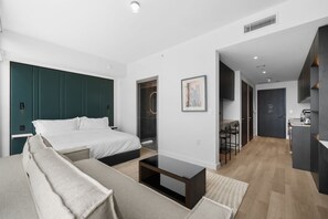 Ein modernes Hotelzimmer mit einem großen Bett, einer Couch, einem kleinen Tisch und einer Küchenzeile im Hintergrund.