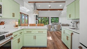 Een moderne keuken met lichtgroene kastjes, een centraal eiland en een zithoek met een bank en salontafel.