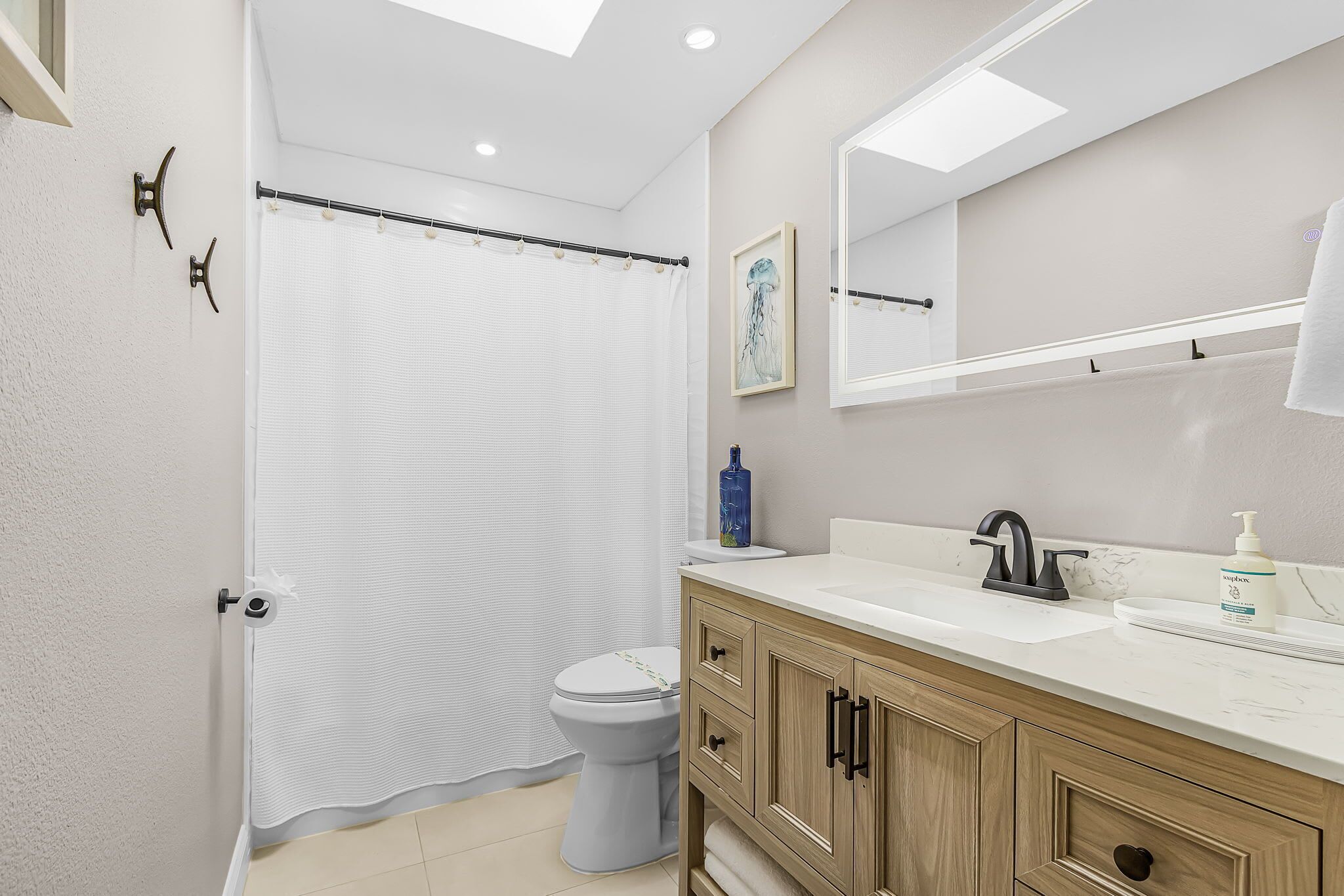 A bathroom with a shower curtain, toilet, sink with soap dispenser, and wooden cabinets.