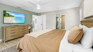 Un dormitorio con cama, cómoda, televisor y ventilador de techo.