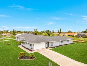 A single-story residential building with a flat roof, surrounded by a well-maintained lawn and a clear sky. - Gorgeous 4 Bedroom Home with Private Pool and Full Kitchen in Rotonda West (Rotonda West)