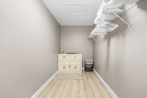 A narrow hallway with a beige wall, a wooden floor, a white ceiling vent, a white metal shelf, a beige cabinet with drawers, and a trash bin. - Gorgeous 4 Bedroom Home with Private Pool and Full Kitchen in Rotonda West (Rotonda West)