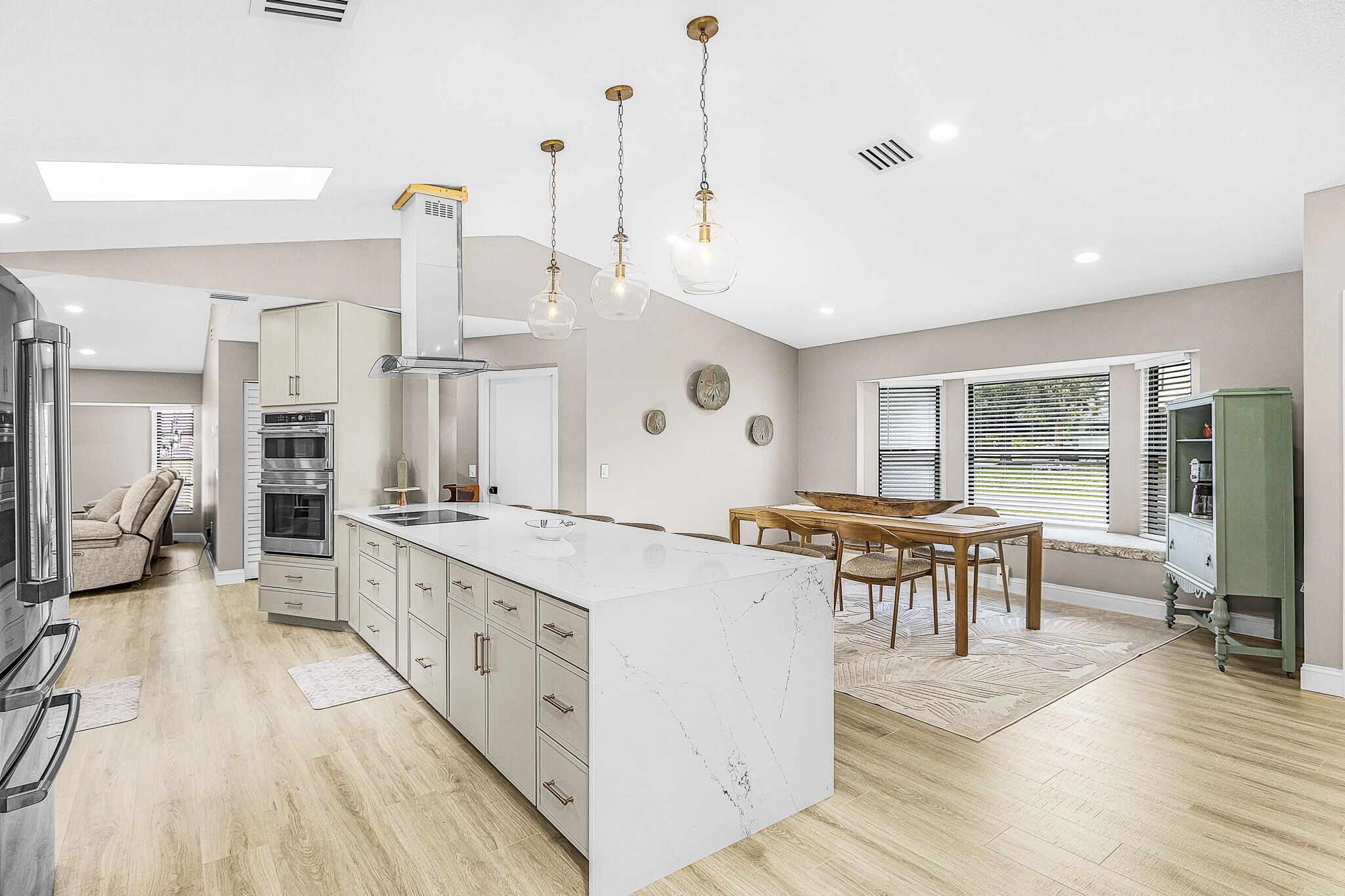 Une cuisine moderne dotée d’un îlot central, d’appareils électroménagers intégrés et de luminaires suspendus.