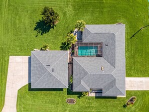 Vista aèria d'una casa de dues plantes amb piscina, envoltada per un jardí ben cuidat i algunes arbres.