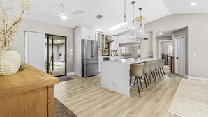 Una cocina moderna con una isla central, taburetes de bar y un ventilador de techo.