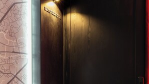 Eine dunkle Holztür, an der Wand daneben eine Karte und ein kleines, beleuchtetes Schild darüber.