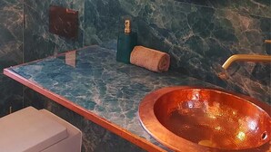 A bathroom with a marble wall, a round mirror, a copper sink, and a towel.