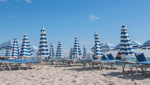 A beach with striped umbrellas and sun loungers. - Chic High-Floor Studio with Intracoastal View (Hallandale Beach)