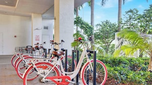 A row of bicycles parked under a covered area with a view of palm trees and greenery. - Chic High-Floor Studio with Intracoastal View (Hallandale Beach)