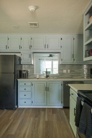 A kitchen with light blue cabinets, a stainless steel refrigerator, a dishwasher, and a tiled backsplash. - The Village 3BR (The Village)