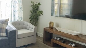 A living room with a grey sofa, a television on a wooden stand, a plant, and a ceiling fan. - The Village 3BR (The Village)