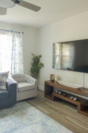A living room with a grey sofa, a television on a wooden stand, a plant, and a ceiling fan. - The Village 3BR (The Village)
