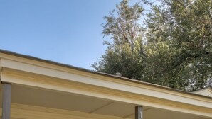 A covered porch with two wicker chairs and a small table, a brick wall, and a clear sky. - The Village 3BR (The Village)