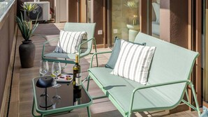 Ein Balkon mit zwei grünen Loungestühlen, einem kleinen Tisch mit einer Weinflasche und Gläsern sowie einer Topfpflanze.