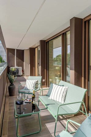 Ein Balkon mit zwei grünen Loungestühlen, einem kleinen Tisch mit einer Weinflasche und Gläsern sowie einer Topfpflanze.