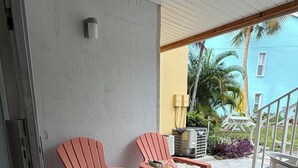 To pinke stole med blomstermønstrede puder på en fliseterrasse, et hvidt bord og en gul bygning i baggrunden.