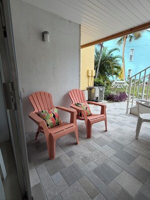 Two pink chairs with floral cushions on a tiled patio, a white table, and a yellow building in the background. - Coastal 2 King BR Retreat Private Beach, Pools & Hot Tub (St. Petersburg)