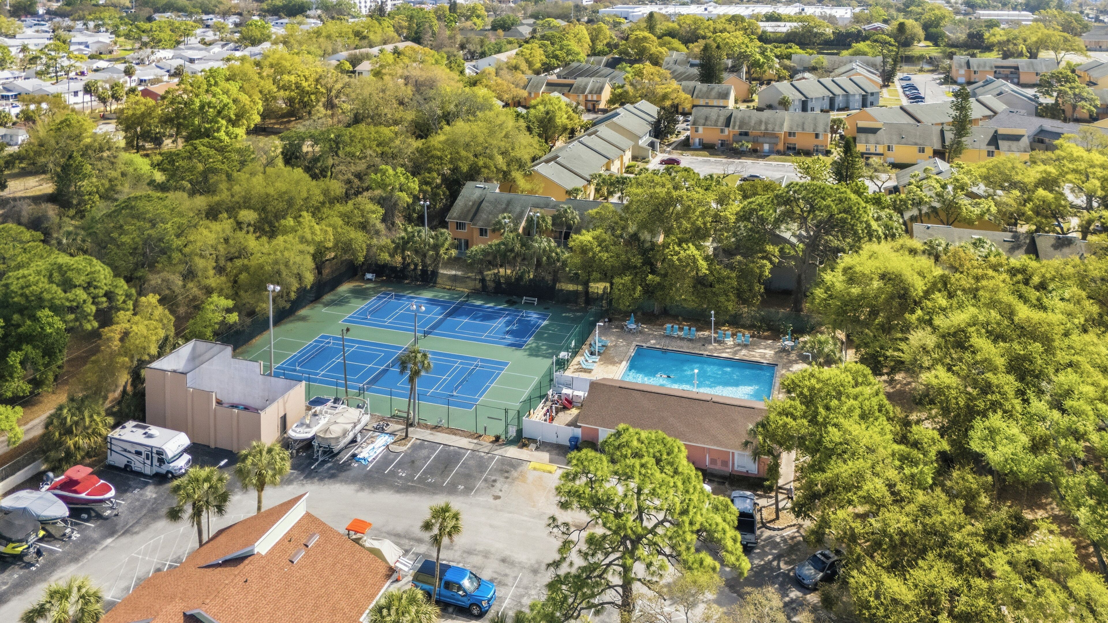 Ein Luftbild eines Wohngebiets mit Tennisplatz, Schwimmbad, Wohnmobilstellplätzen und umgebender Bepflanzung.