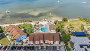 Oversigtsbillede af en ejendom ved kysten med swimmingpool, adgang til stranden og parkerede biler.