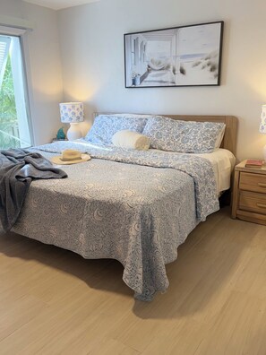A bedroom with a bed, bedside tables, a window, and a wall-mounted painting. - Coastal 2 King BR Retreat Private Beach, Pools & Hot Tub (St. Petersburg)