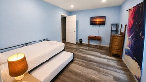 Ein Schlafzimmer mit Bett, Nachttischlampe, Holzboden, einem Bild an der Wand und einer Tür zu einem anderen Raum.