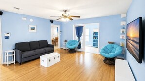 Ein Wohnzimmer mit grauem Sofa, zwei blauen Sesseln, einem weißen Couchtisch und einem Deckenventilator.